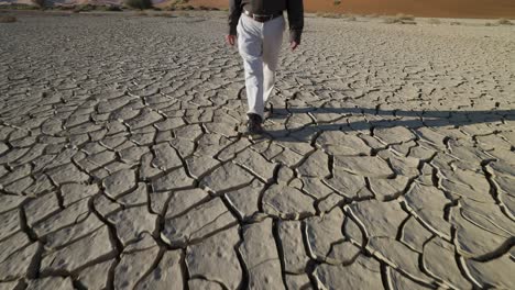 cambio climático. vista de cultivo de un granjero devastado caminando a través de la superficie de barro agrietado de una presa seca debido a la sequía del cambio climático y el calentamiento global