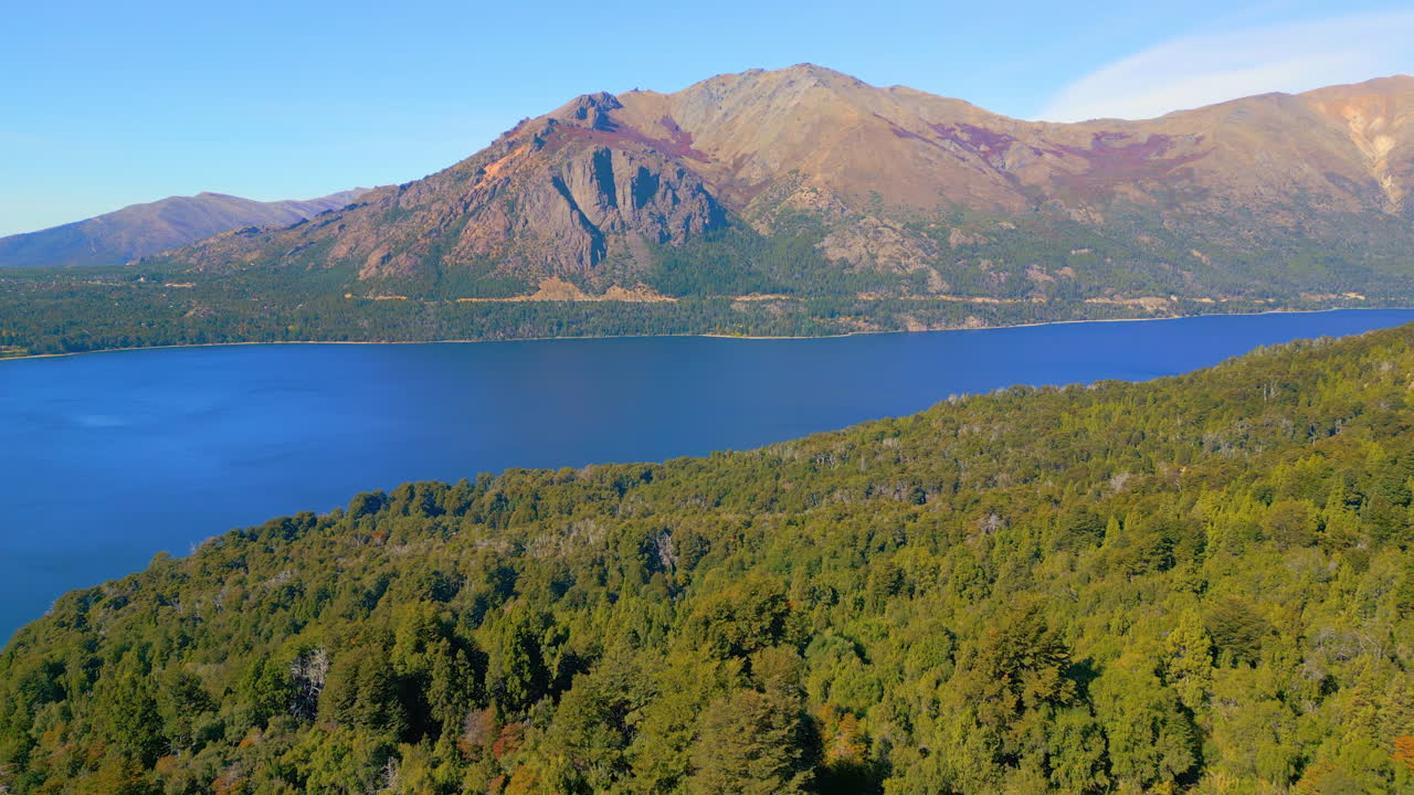 Vista aerea panoramica di una costa boscosa, un lago blu e montagne maestose.