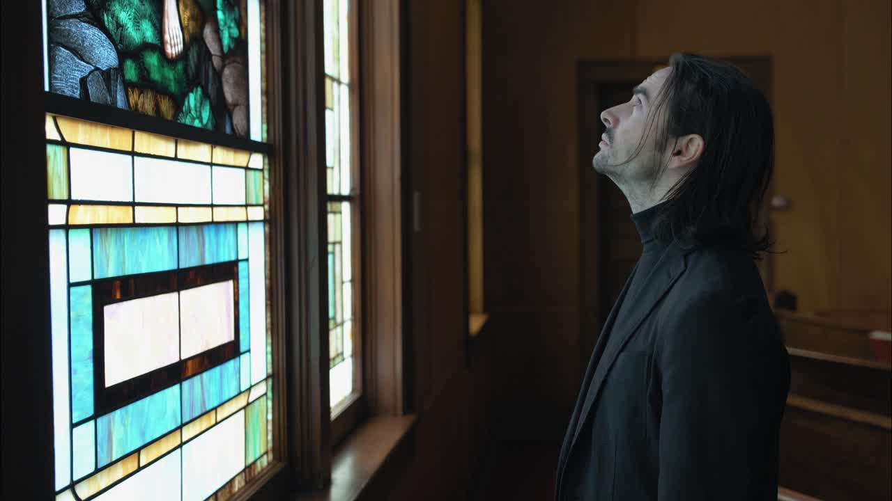 A Christian man, priest, preacher, pastor looking at stained glass window creating a cinematic and contemplative mood