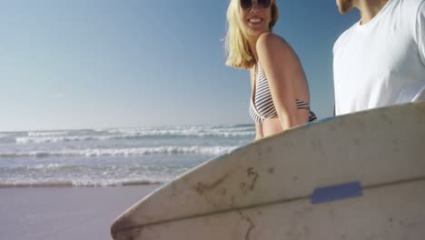 pareja caminando juntos con una tabla de surf en la playa