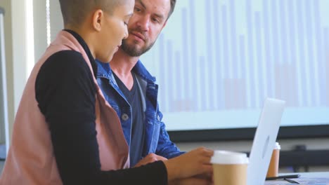 Side-view-of-young-business-colleagues-discussing-over-laptop-in-modern-office-4k