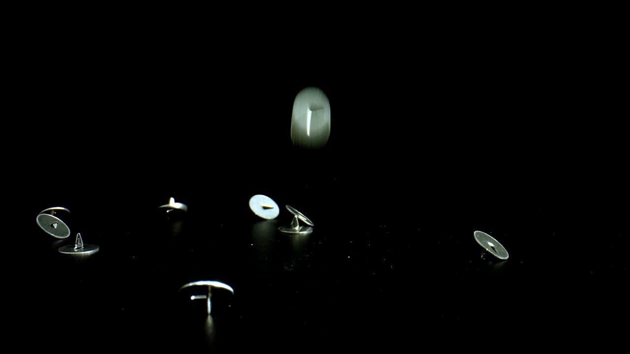 검은색 반사 표면에 천천히 떨어지는 금속 밀기 핀