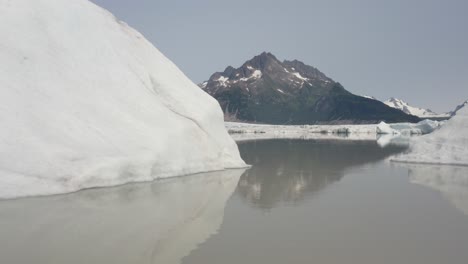 Flying-low-over-a-lake-through-icebergs-by-the-mountains-of-Alaska--Low-aerial