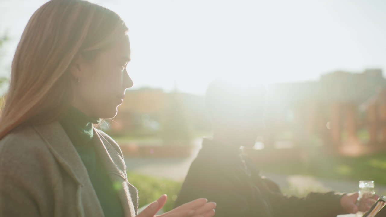 Side view of lady handing snack to kid outdoors as he happily collects it, natural sunlight glowing in background creating warm atmosphere of care, family support, and joyful bonding