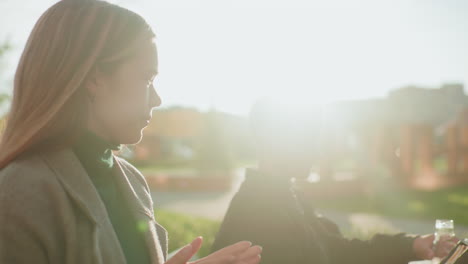side view of lady handing snack to kid outdoors as he happily collects it, natural sunlight glowing in background creating warm atmosphere of care, family support, and joyful bonding