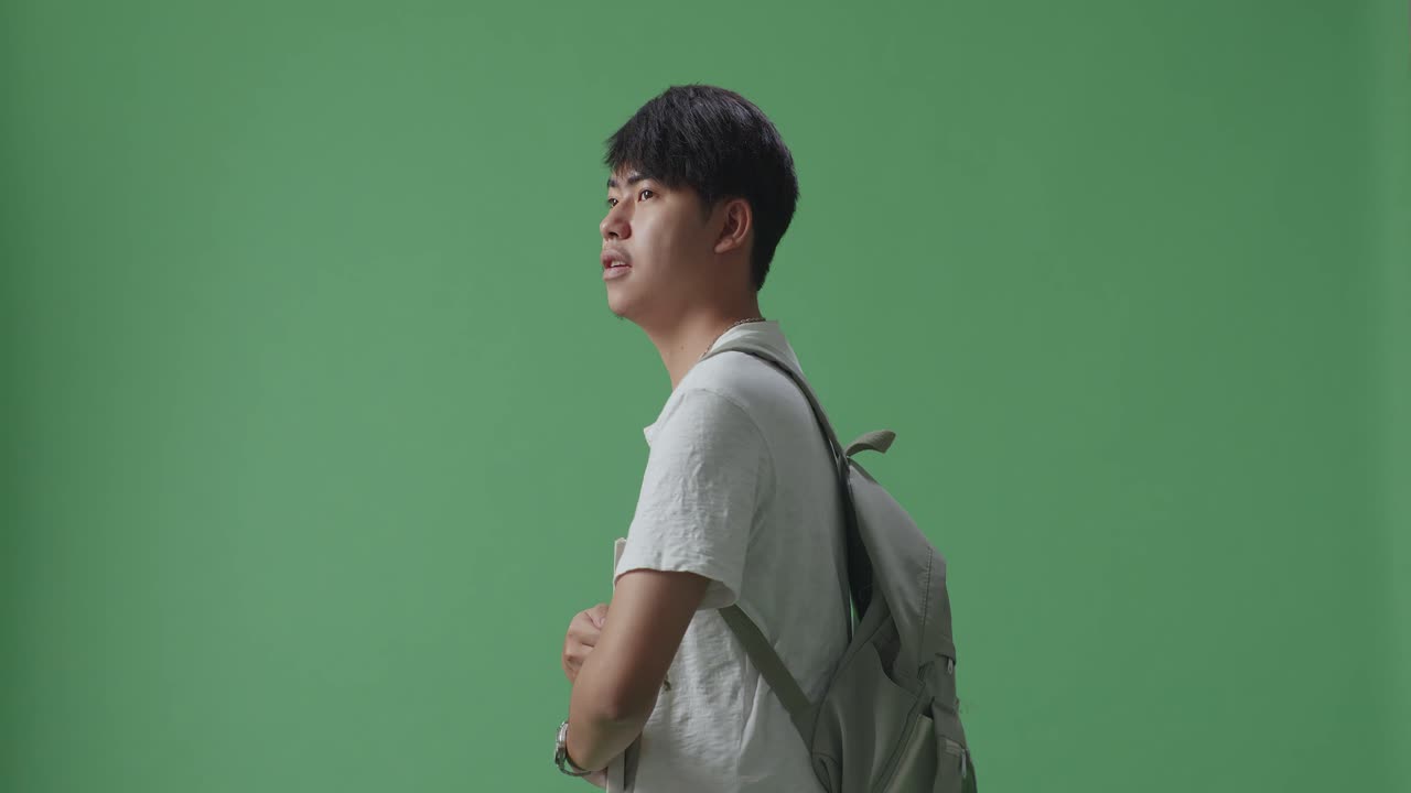 vista lateral de un estudiante asiático con un libro en la mano y caminando en el estudio de pantalla verde