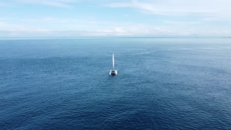 flying towards and over a small yacht as it sails in a calm, flat ocean