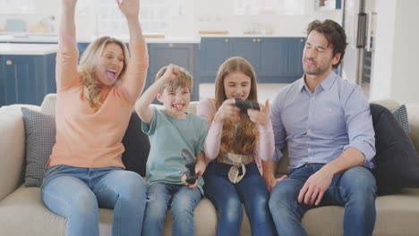 padres divirtiéndose sentados en el sofá con los niños en casa jugando en la consola de juegos