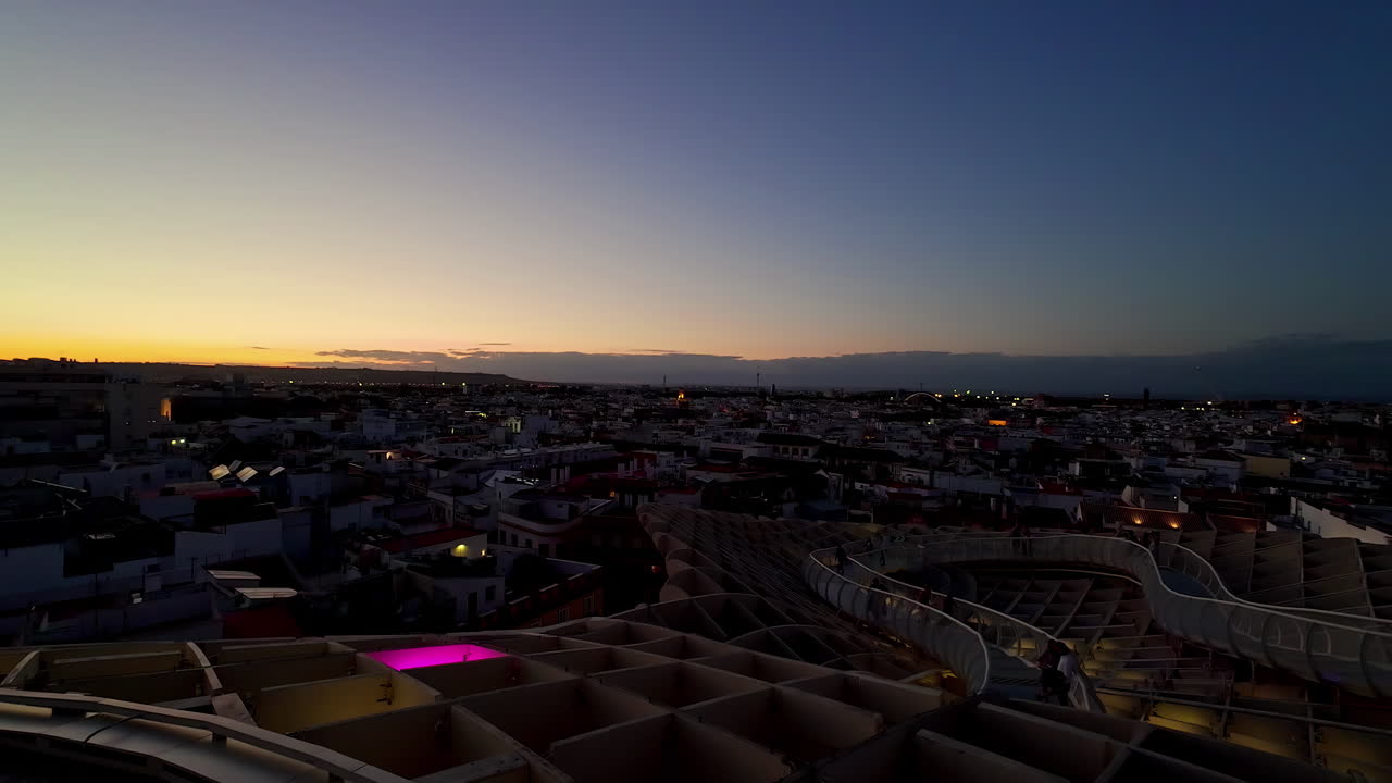 시빌리아의 어두움이 내려오고, 도시의 불빛이 박거리며, 낮에서 밤으로의 전환을 포착합니다.