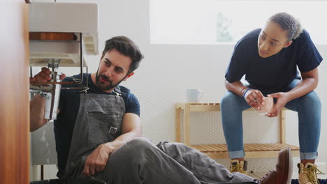 Plomero-Masculino-Enseñando-A-Una-Aprendiz-A-Arreglar-Un-Lavabo-Con-Fugas-En-El-Baño-De-Su-Casa