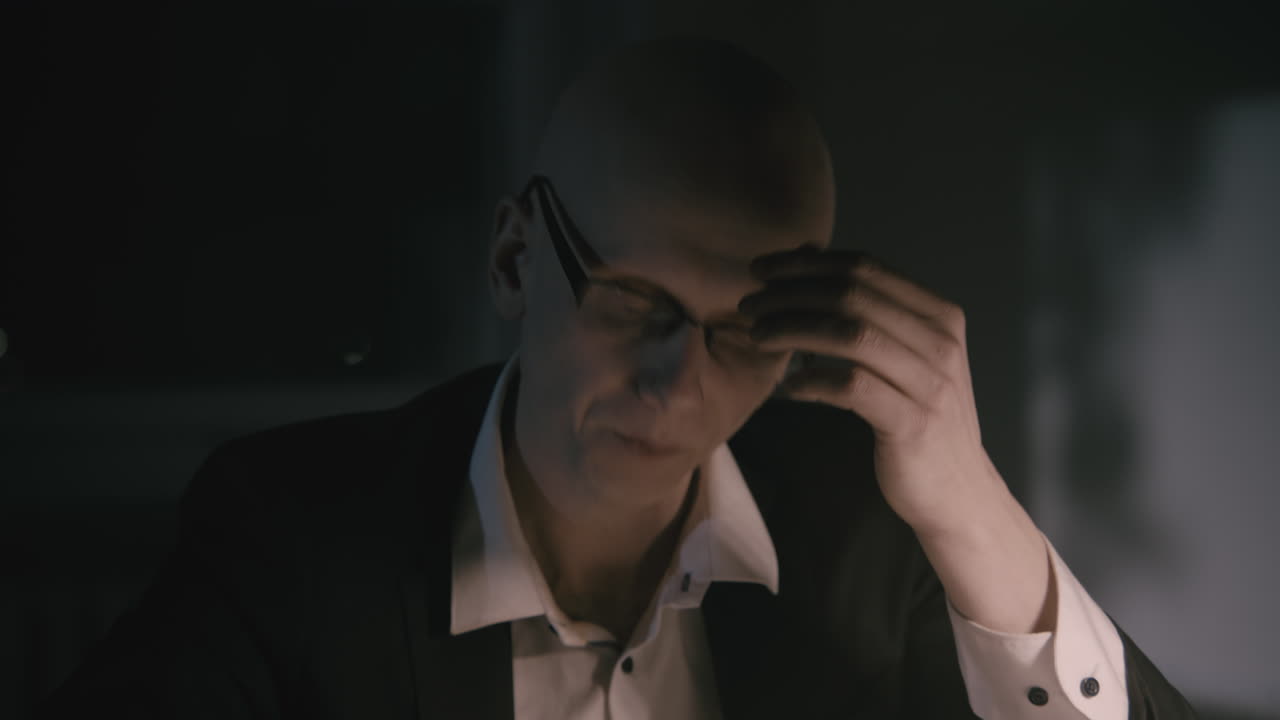 Pale bald accountant looks through the tax papers in the weird room at night
