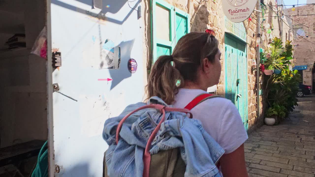 Giovane donna con lo zaino che cammina attraverso una soleggiata via del centro storico
