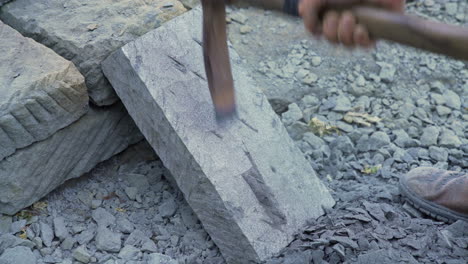 handheld shot of a handheld pick being used by a stone craftsman to shape a stone slab, outside in bright daylight in the city of ancud, chiloe island