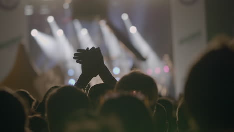 view from behind of hands hold smartphone among people at rave party with light