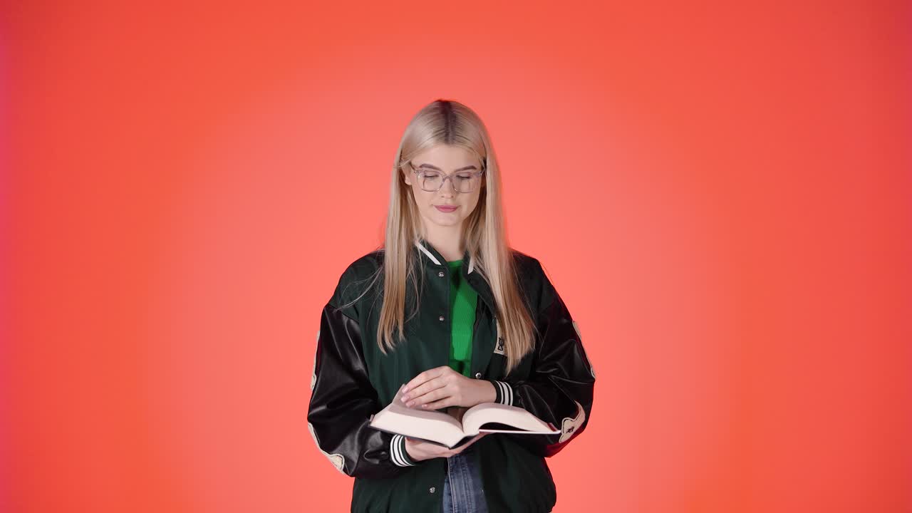 Giovane studentessa bionda che legge e sfoglia un libro, ritratto in studio colorato