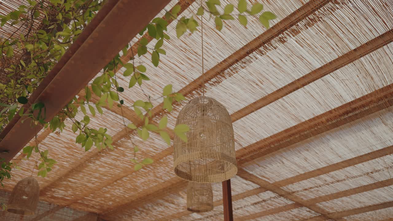 Natural wicker lamps hanging from bamboo roof with green leaves