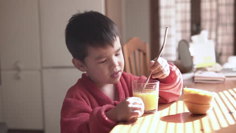 Asian-child-having-natural-organic-freshly-squeezed-orange-juice-for-breakfast-in-his-pajamas