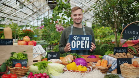 smiling farmer holding open sign at market stall