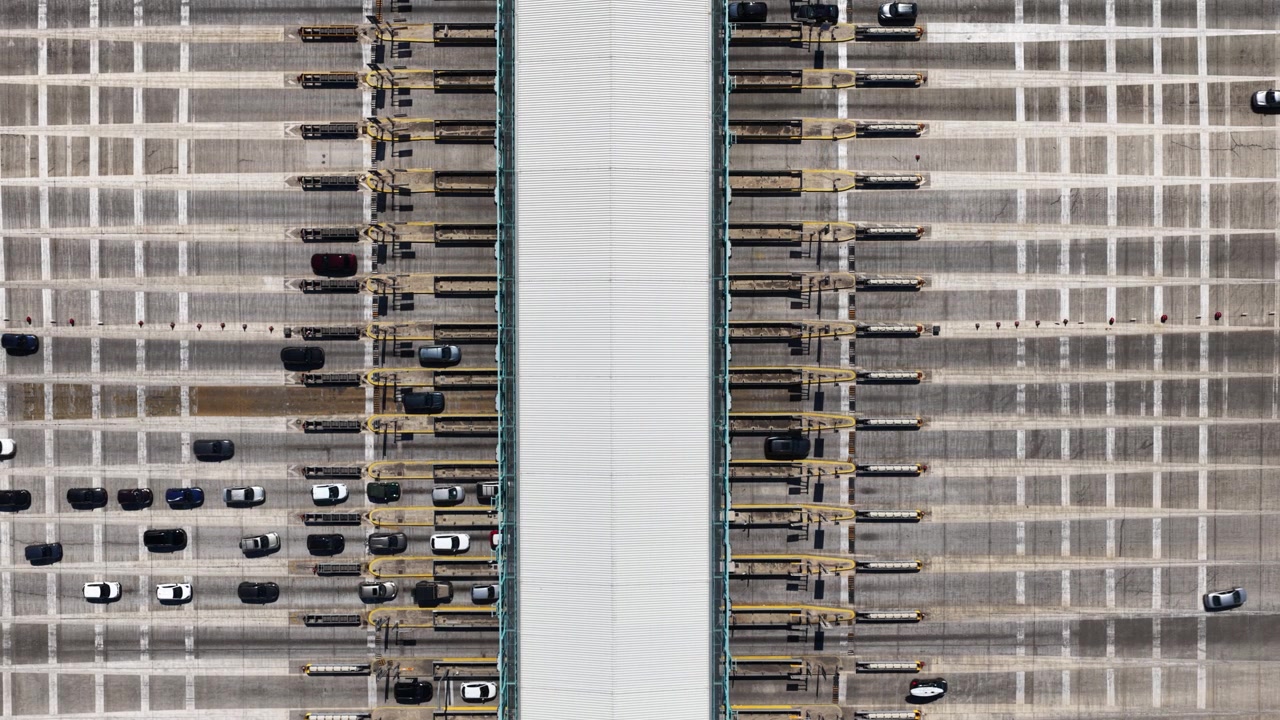 High-angle, symmetrical view of cars and vehicles passing through a busy toll plaza on a multi-lane highway, representing transportation infrastructure and daily commuter travel