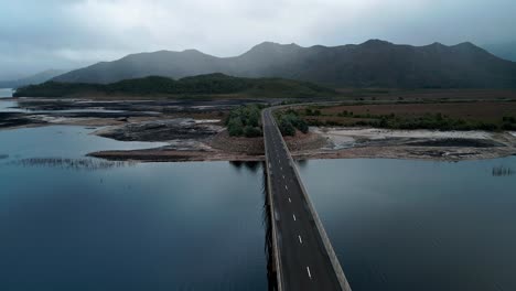 backward drone shot of lake burbury with beautiful landscape and a bridge in foreground in tasmania, australia under a cloudy day