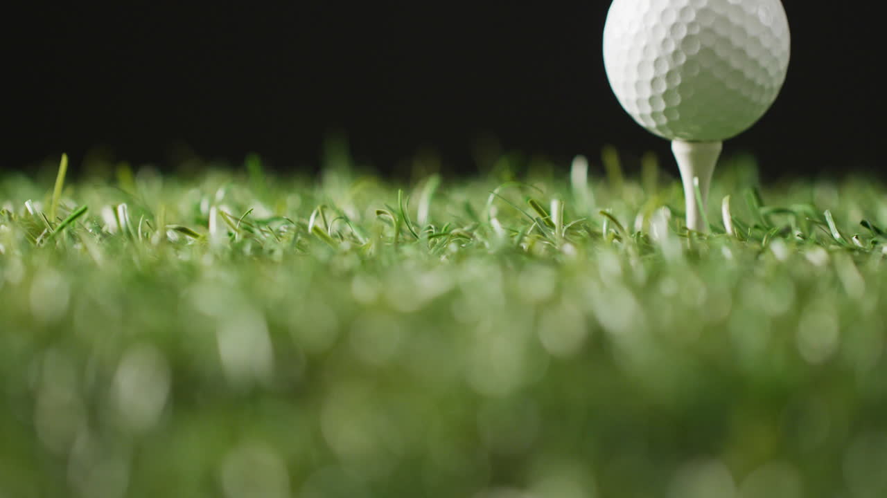 잔디와 검은 바탕에 있는 골프 티와 공의 클로즈업, 복사 공간, 슬로우 모션