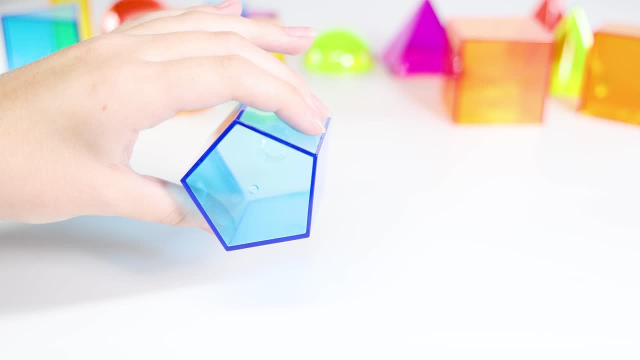 Hands manipulate transparent geometric shapes on a white surface, showcasing vibrant colors and educational exploration