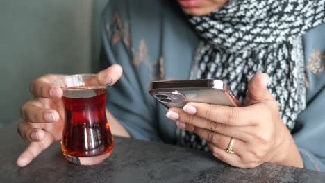 woman in hijab drinking tea and using her phone