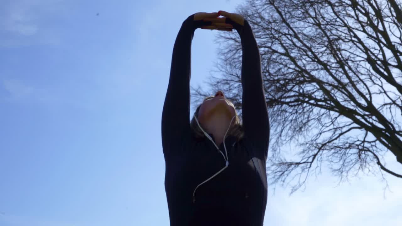 공원에서 손을 펴고 있는 이어폰을 쓴 운동선수 소녀