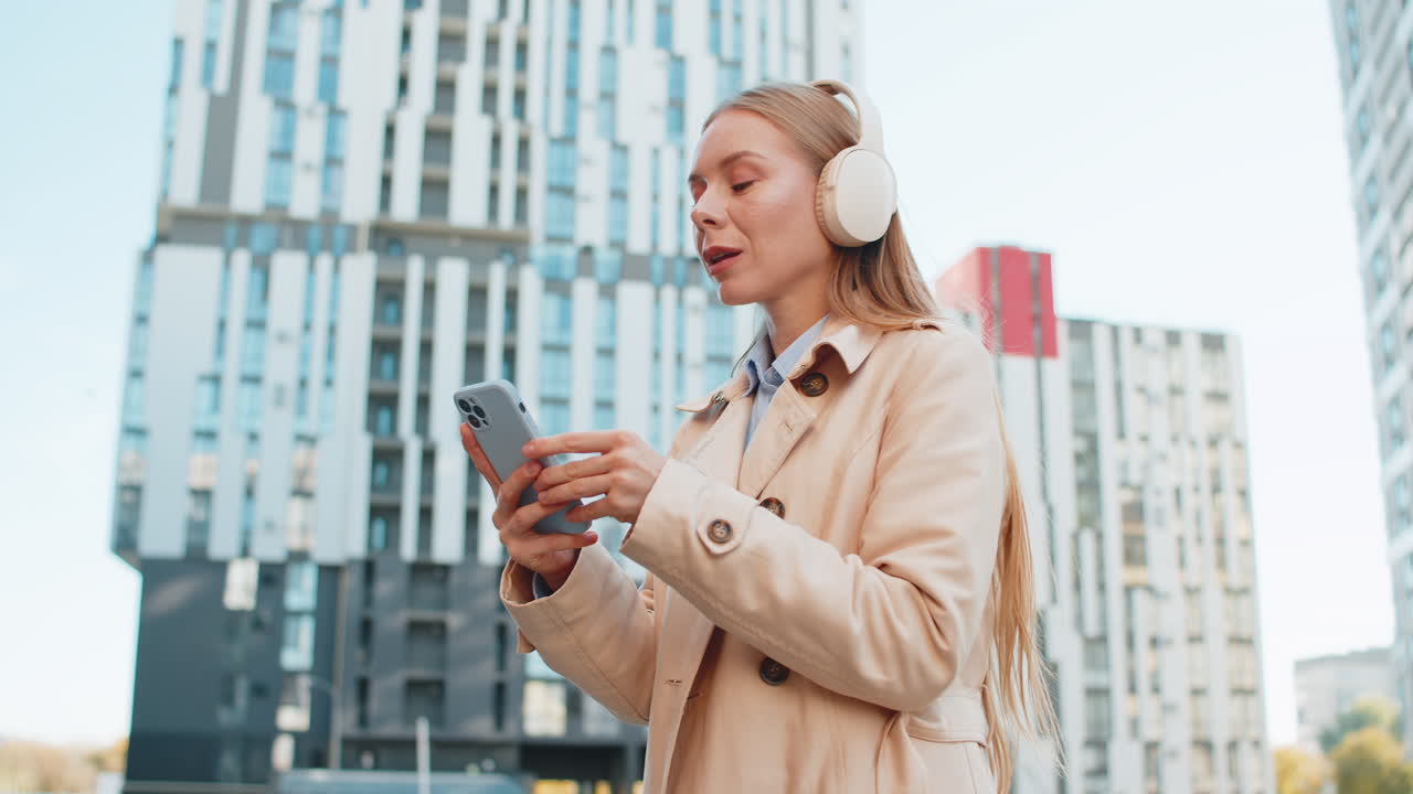 Una donna d'affari matura felice con le cuffie che ascolta la sua musica energetica preferita sullo smartphone per strada