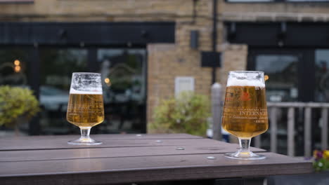 two glasses of beer on a bench in front of a pub in a beer garden