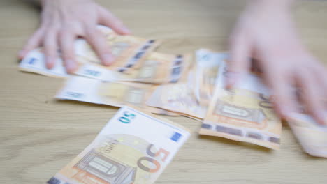 Man-hands-making-a-pile-of-paper-money-bills,-on-a-wooden-table-and-picking-them-up