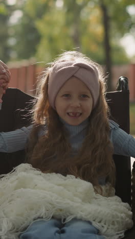 toothless little girl smiles rotating wheel of medical equipment and holding hand of mom. woman enjoys spring walk in park with daughter closeup