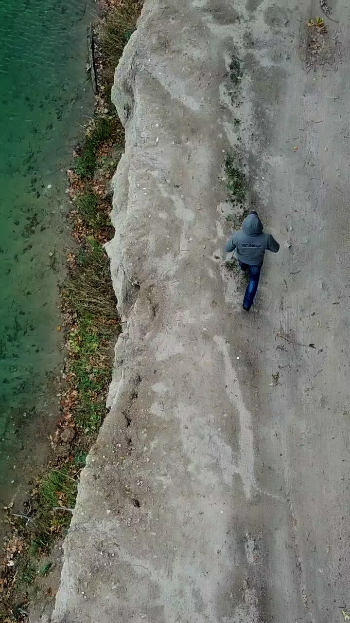 Man walking along lake. Aerial view of man walking along lake with forest Vertical video