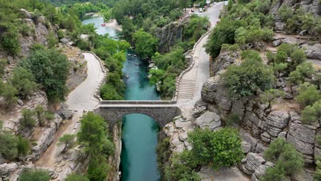 aerial view of a stone arch bridge over a turquoise river in a canyon