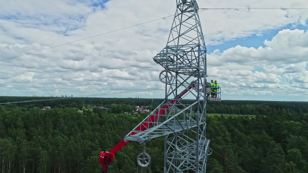 Drone rotation around high voltage electricity tower and technicians in their uniform inspecting technicalities using lifting crane
