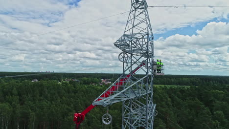 drone rotation around high voltage electricity tower and technicians in their uniform inspecting technicalities using lifting crane