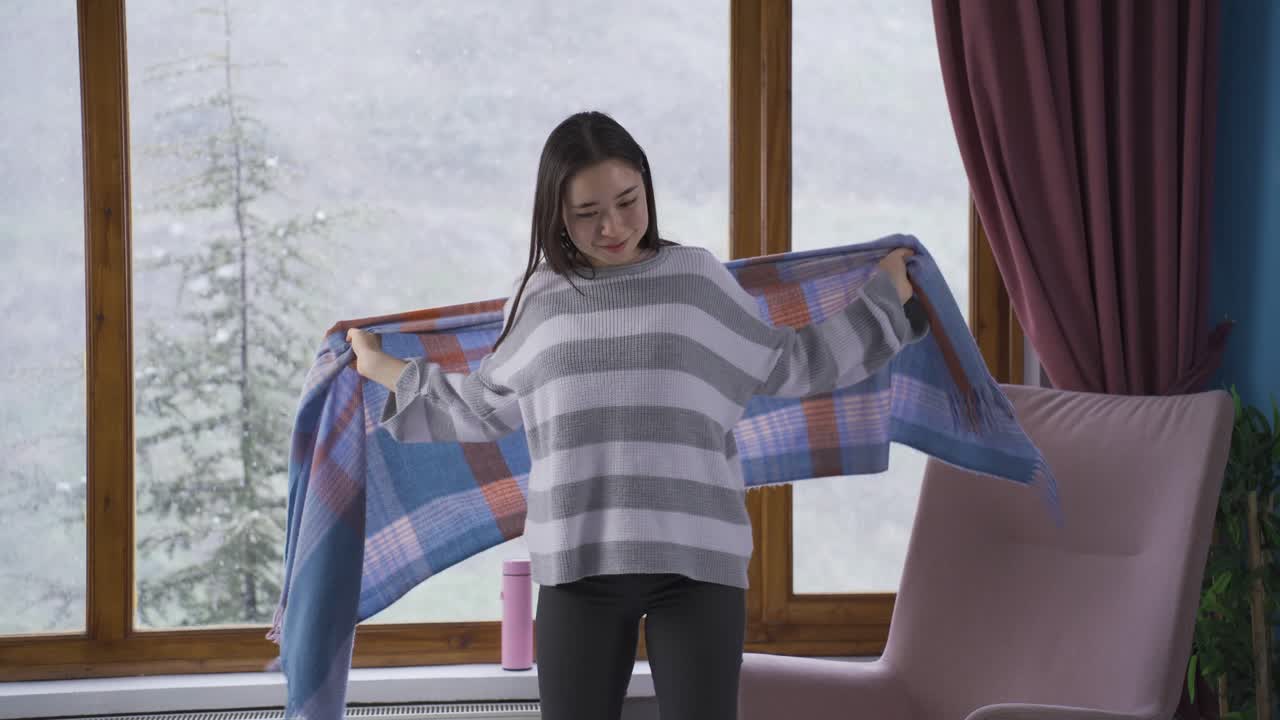 젊은 아시아 여성이 창밖을 바라보며 내리는 눈을 지켜보고 있습니다.