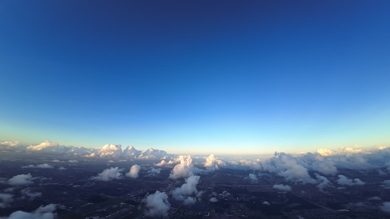 Rays of bright setting sun light the soft fluffy clouds. Footage from FPV drone high in the sky over the city landscape.