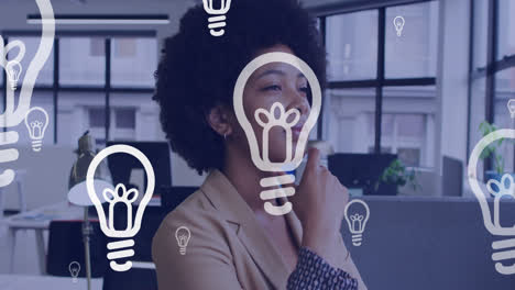 animación de iconos de bombillas sobre mujer de negocios afroamericana pensando en la oficina