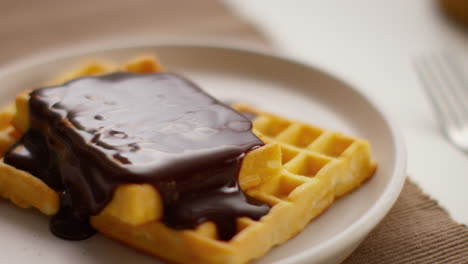 close up melted chocolate sauce on stack of waffles on plate