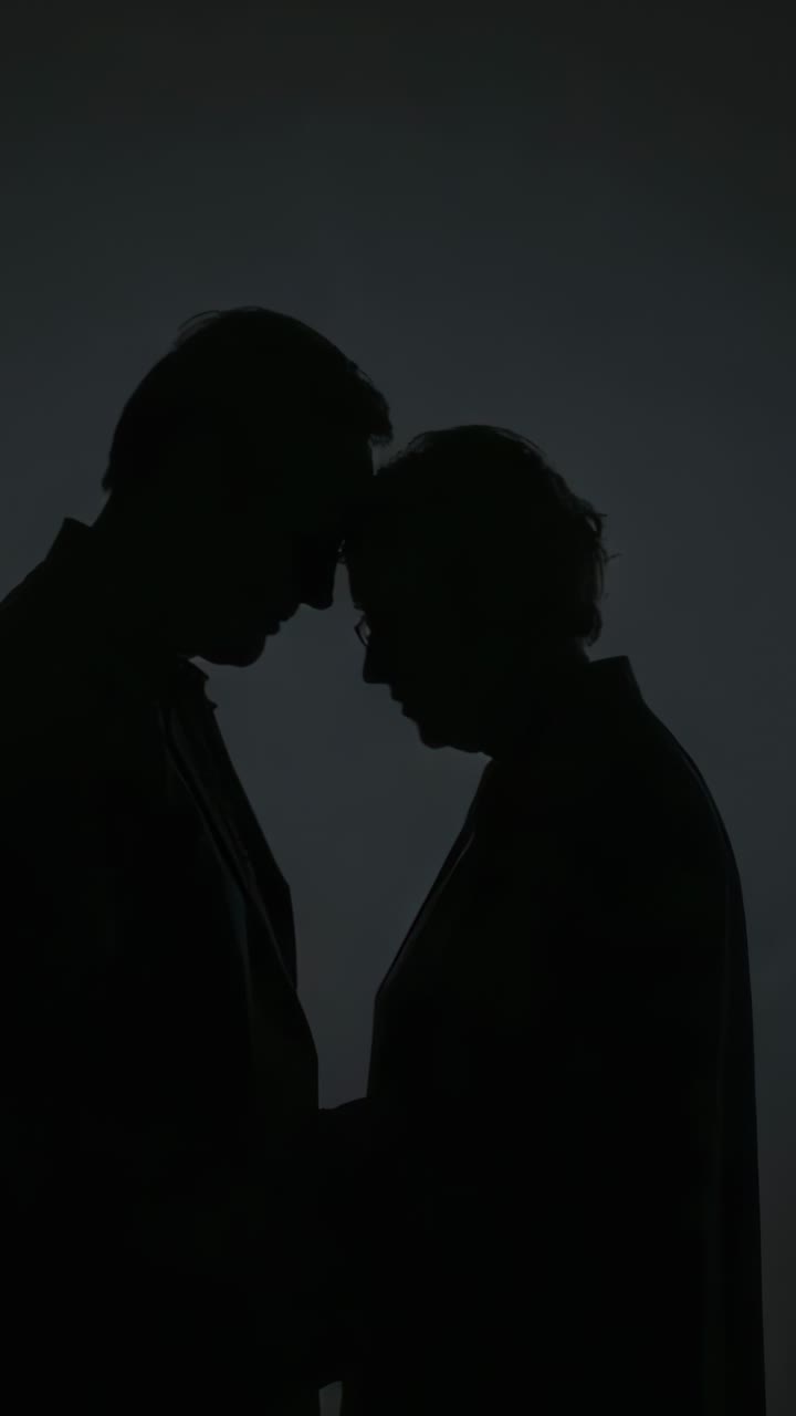 Vertical video: Leaning couple touching foreheads walking forward in studio, holding joined hands