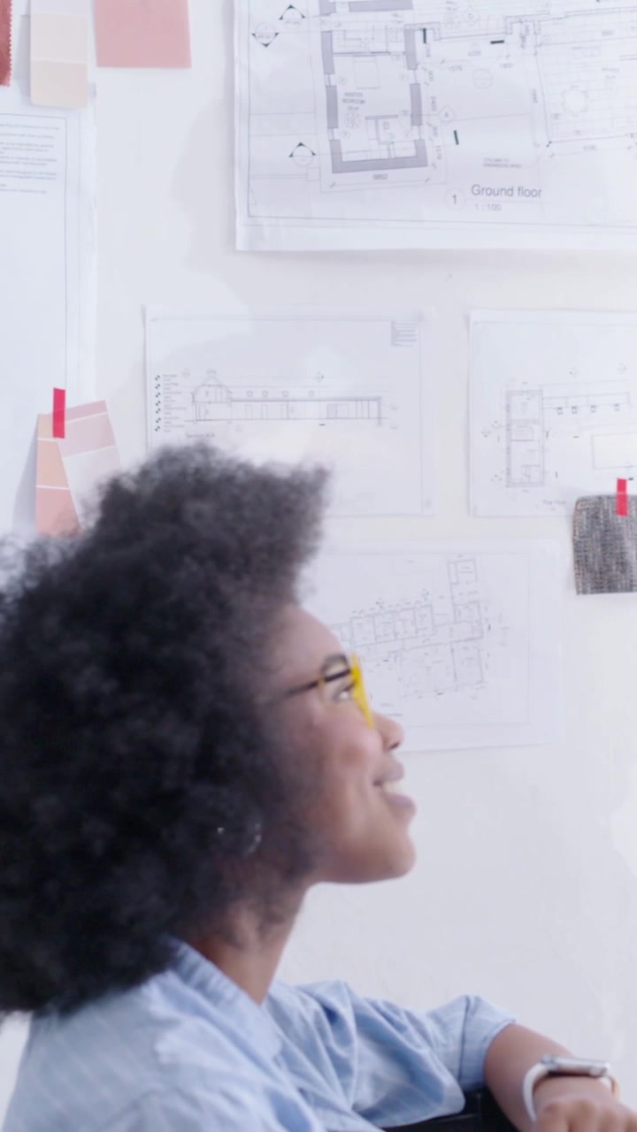 Video verticale: Designer che si gira osservando un collega che mostra una planimetria su tablet in studio per una revisione.