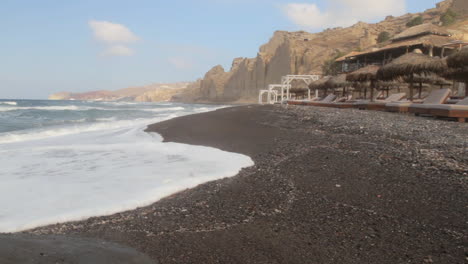 tracking shot of a black sand beach with a beach resort in the foreground and white volcanic cliff formations in the background