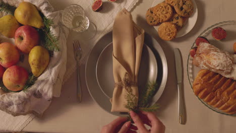 mujer irreconocible decorando una servilleta con una ramita de abeto para la cena de navidad