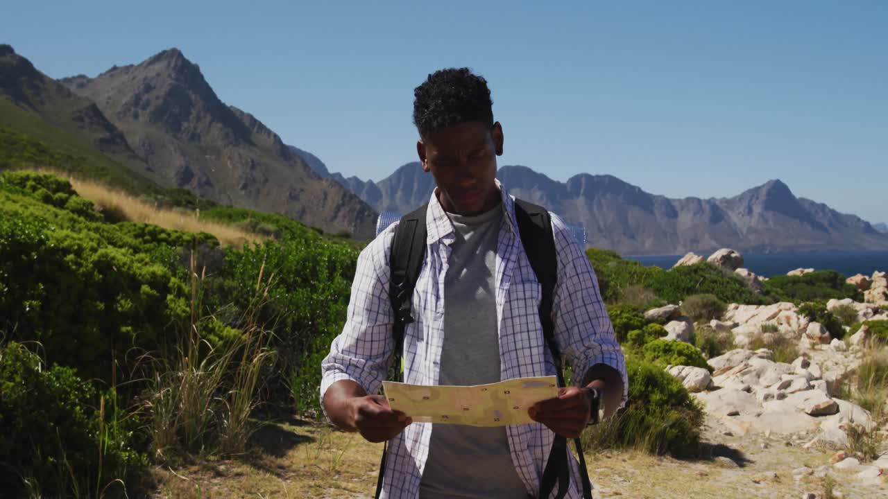 hombre afroamericano haciendo senderismo leyendo un mapa en el campo costero