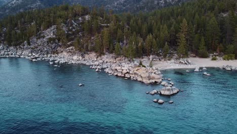 clockwise drone shot of three people sitting on the huge rocks at chimney beach on the shore of lake tahoe watching the sunset