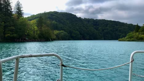 Tilt-Up-Boat-View-of-Bright-Blue-Plitvice-Lakes-with-Shady-Dense-Forest-on-Background