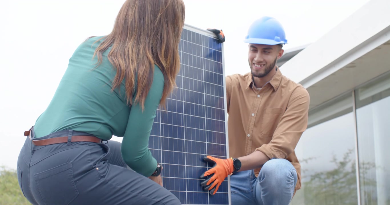 Afroamerikanskt team påbörjar installationen, knäböjer och lyfter en solpanel på däck med handskar som skydd mot solen