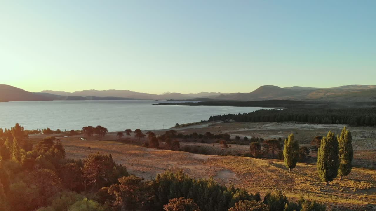 Aerial view near Alumine lake in Neuquén Province at sunset showing forest and mountains bathed in orange light.