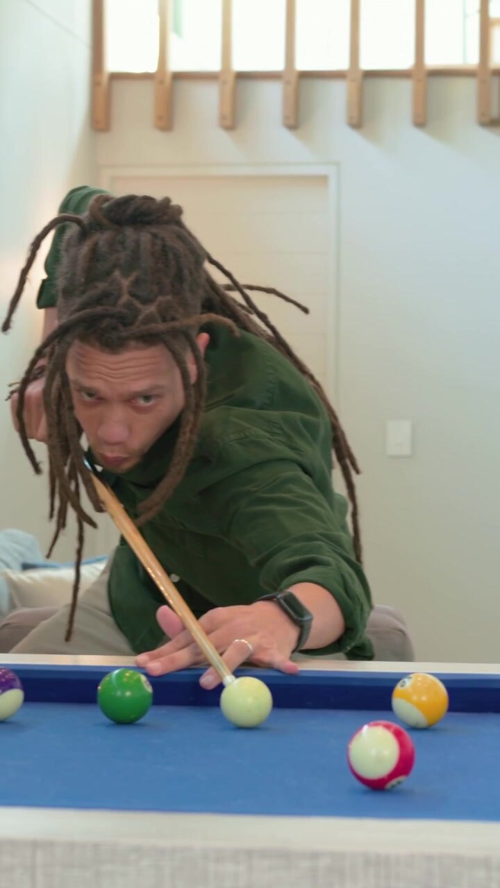 Vertical video: Approaching man with dreads in green shirt, chalking cue and playing pool at home